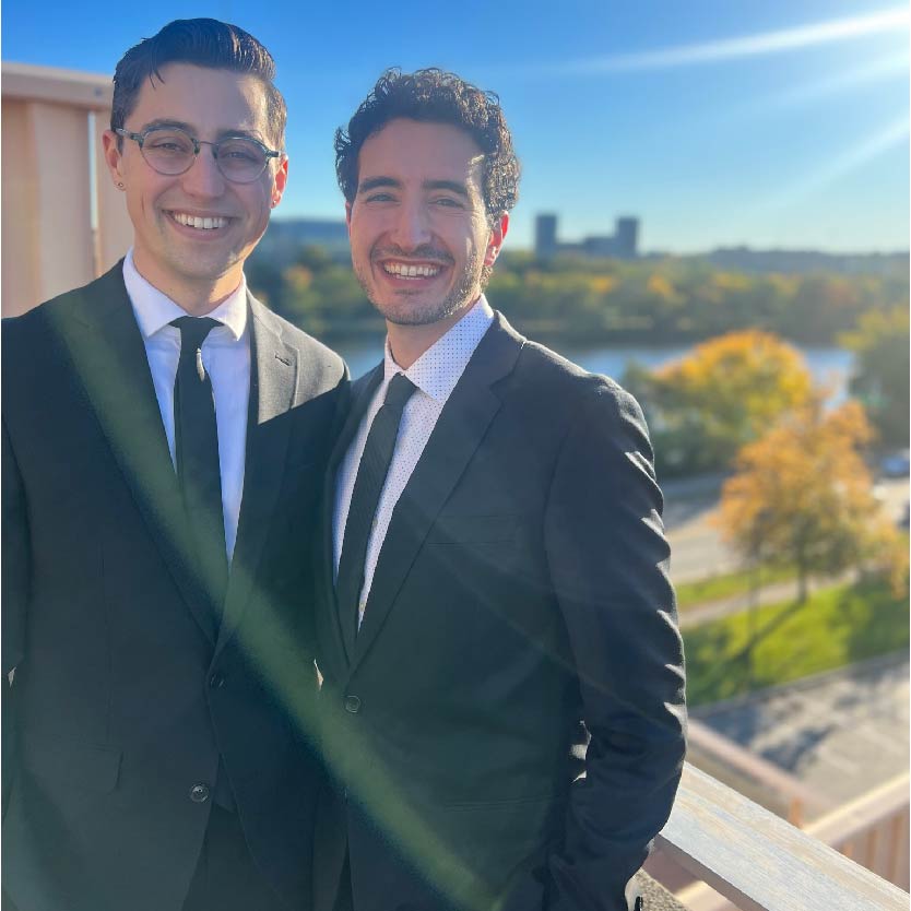 Darius and Tom wearing suits on a balcony
